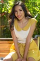 A woman sitting on a wooden bench in a yellow dress.